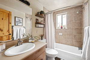 Bathroom with a textured ceiling, shower / tub combo, toilet, and vanity