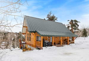 Snow covered rear of property with log siding, a porch, metal roof, and a standing seam roof