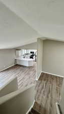 Unfurnished living room with lofted ceiling, wood finished floors, a textured ceiling, baseboards, and a sink