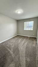 Unfurnished room with baseboards, a textured ceiling, and dark carpet