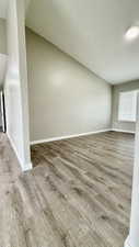 Empty room featuring vaulted ceiling, wood finished floors, and baseboards