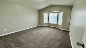 Spare room featuring vaulted ceiling, dark colored carpet, and baseboards