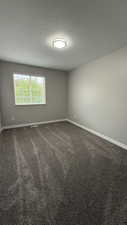 Spare room with baseboards, dark colored carpet, and a textured ceiling