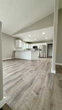 Unfurnished living room with baseboards, recessed lighting, light wood-type flooring, and vaulted ceiling