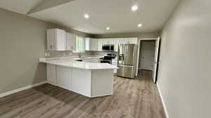 Kitchen with appliances with stainless steel finishes, a peninsula, a sink, baseboards, and light wood-style flooring