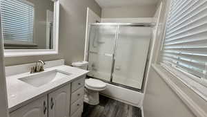 Bathroom with wood finished floors, bath / shower combo with glass door, healthy amount of natural light, and vanity