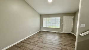 Spare room featuring vaulted ceiling, wood finished floors, and baseboards