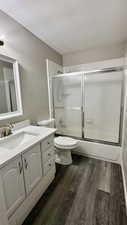 Full bathroom with a textured ceiling, wood finished floors, enclosed tub / shower combo, toilet, and vanity