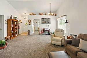 Carpeted living room featuring lofted ceiling and a notable chandelier