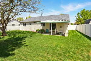 Rear view of property with a yard, a patio area, roof with shingles, and a fenced backyard