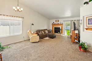 Carpeted living room with high vaulted ceiling, a tiled fireplace, baseboards, and a notable chandelier