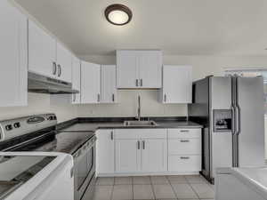 Kitchen with under cabinet range hood, stainless steel appliances, a sink, white cabinetry, and light tile patterned floors
