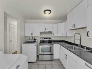 Kitchen with stainless steel electric range, a sink, under cabinet range hood, light tile patterned floors, and white cabinets