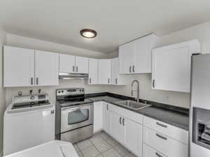 Kitchen with washer / dryer, stainless steel appliances, under cabinet range hood, a sink, and white cabinetry