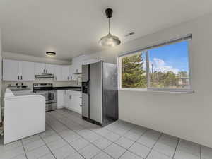 Kitchen with refrigerator with ice dispenser, stainless steel range with electric stovetop, washer / dryer, white cabinets, and pendant lighting