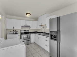 Kitchen with stainless steel appliances, a sink, under cabinet range hood, washer and dryer, and light tile patterned flooring