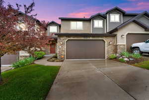 Townhome / multi-family property with stone siding, stucco siding, concrete driveway, and an attached garage