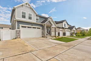 Craftsman-style house featuring stone siding, an attached garage, concrete driveway, a residential view, and fence