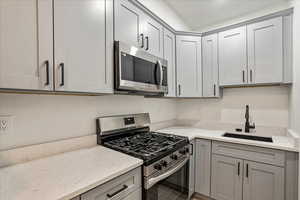 Kitchen with appliances with stainless steel finishes, a sink, gray cabinetry, and light stone counters