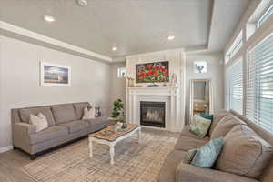 Living area featuring a textured ceiling, light wood-type flooring, a fireplace, recessed lighting, and baseboards