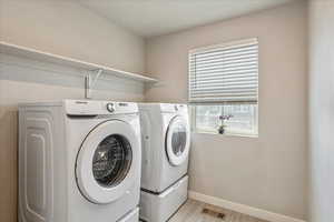 Laundry area with washing machine and dryer, light wood-type flooring, and baseboards