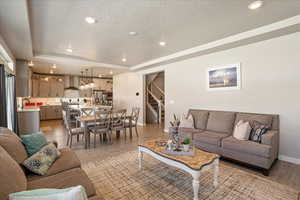 Living area with baseboards, stairs, a raised ceiling, a textured ceiling, and light wood finished floors