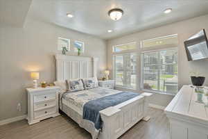 Bedroom featuring baseboards, multiple windows, light wood-style flooring, a textured ceiling, and recessed lighting