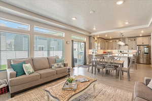 Living room featuring a textured ceiling, plenty of natural light, light wood-type flooring, recessed lighting, and a tray ceiling