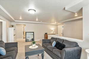 Living room featuring light colored carpet, a raised ceiling, baseboards, recessed lighting, and a textured ceiling