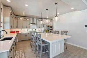 Kitchen with a sink, wall chimney exhaust hood, appliances with stainless steel finishes, a kitchen breakfast bar, and light wood-style floors