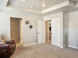 Sitting room with a tray ceiling, light colored carpet, baseboards, a textured ceiling, and recessed lighting