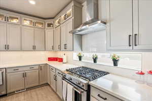 Kitchen featuring gas stove, wall chimney range hood, decorative backsplash, light countertops, and recessed lighting