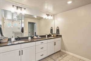 Full bath with baseboards, tile patterned floors, double vanity, a walk in shower, and a textured ceiling