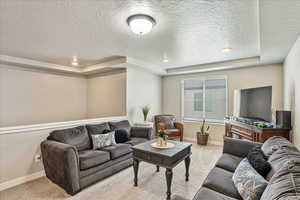 Living room with a tray ceiling, a textured ceiling, baseboards, and carpet floors