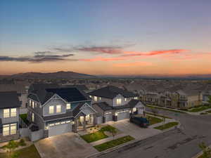 View of front of property featuring a garage, a residential view, stone siding, concrete driveway, and fence