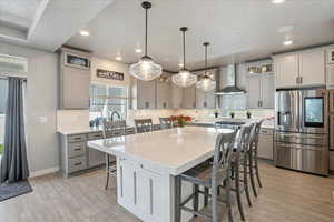 Kitchen featuring stainless steel fridge with ice dispenser, wall chimney range hood, gray cabinetry, a kitchen breakfast bar, and backsplash
