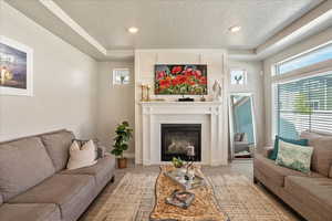 Living room with a textured ceiling, wood finished floors, a brick fireplace, and recessed lighting