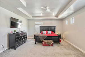 Carpeted bedroom featuring a tray ceiling, multiple windows, a textured ceiling, baseboards, and a ceiling fan