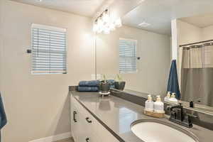 Full bath featuring plenty of natural light, double vanity, a textured ceiling, baseboards, and a shower with shower curtain