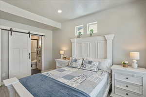 Bedroom with a barn door, baseboards, ensuite bath, and wood finished floors