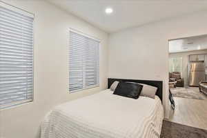 Bedroom featuring freestanding refrigerator, wood finished floors, multiple windows, and recessed lighting