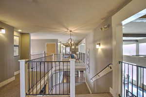 Hall with baseboards, a notable chandelier, an upstairs landing, and carpet