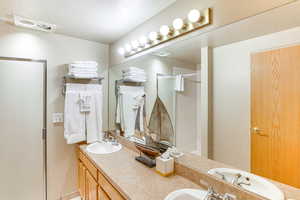 Full bath featuring a textured ceiling, double vanity, a sink, and a shower stall
