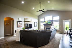 Living room with a ceiling fan, high vaulted ceiling, arched walkways, wood finished floors, and a fireplace