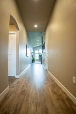 Hallway with arched walkways, wood finished floors, vaulted ceiling, baseboards, and recessed lighting