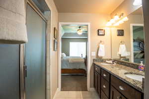 Ensuite bathroom with ceiling fan, tile patterned floors, a stall shower, double vanity, and baseboards