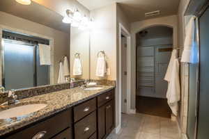 Full bathroom with tile patterned floors, a shower stall, double vanity, and baseboards