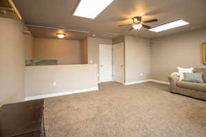 Unfurnished room featuring a ceiling fan, carpet flooring, baseboards, and a skylight