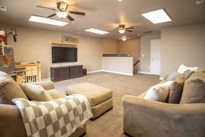 Living room with a ceiling fan, carpet flooring, baseboards, and a skylight