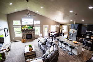 Carpeted living room featuring recessed lighting, a stone fireplace, a ceiling fan, baseboards, and high vaulted ceiling
